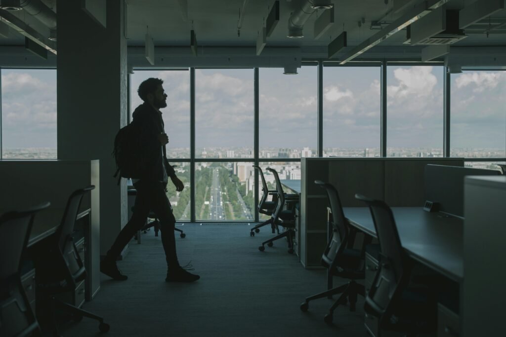 pexels photo 5483161 5483161 Silhouette of a man walking through a modern office interior with large windows and an urban city view.